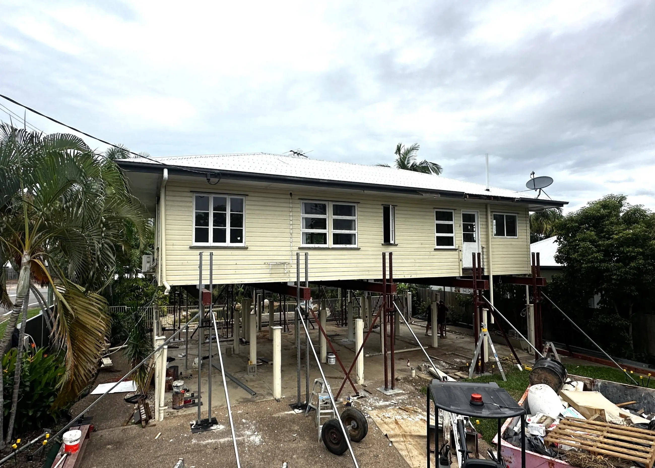 A weatherboard house held on steel props while its new lower level is being constructed