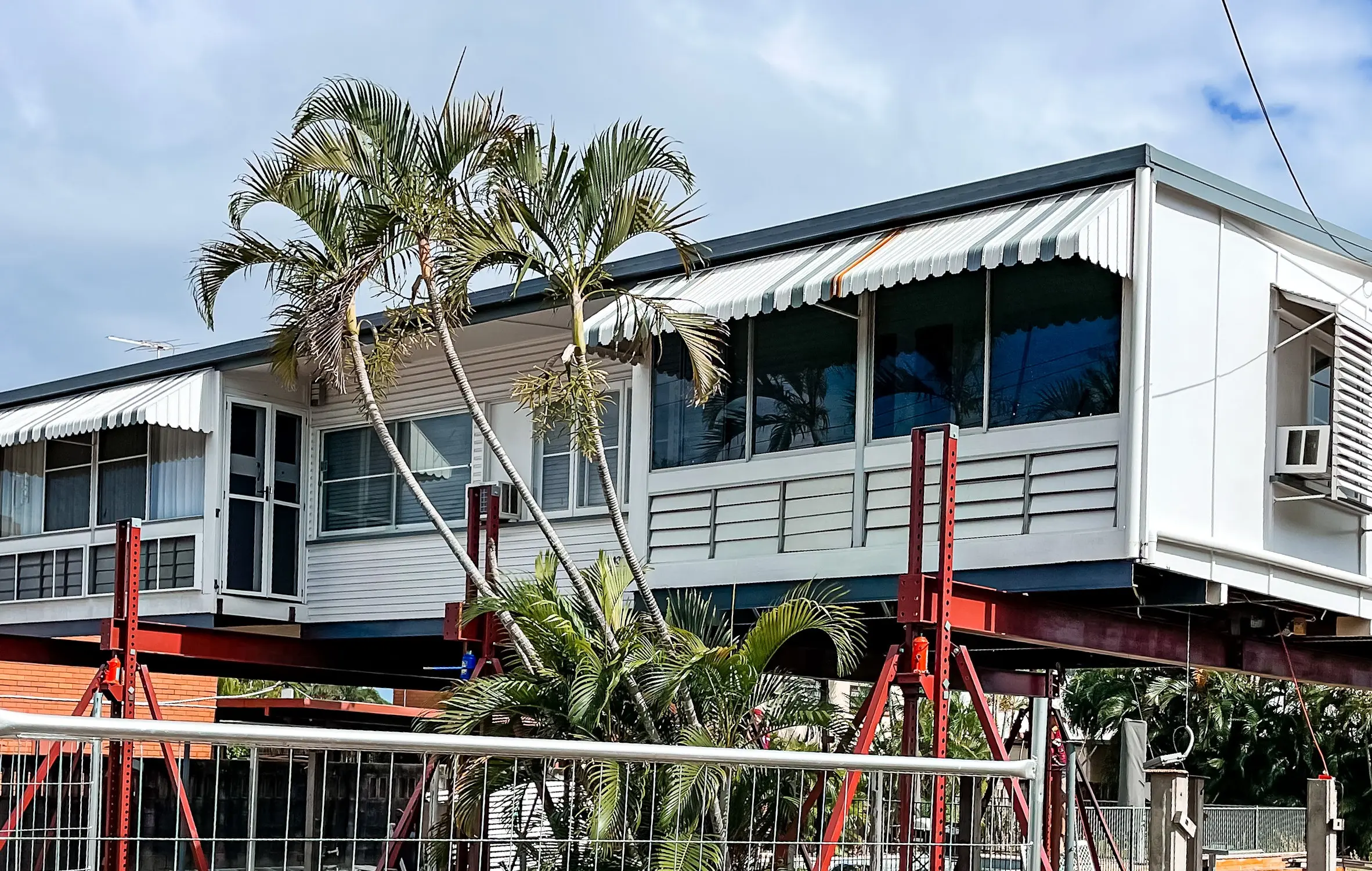 A house standing high on steel props above an excavated pad, mid-raise