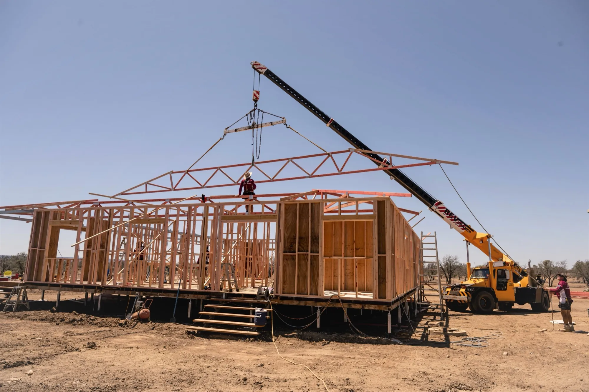 Roof trusses being craned onto a new frame on a red-dirt block out west