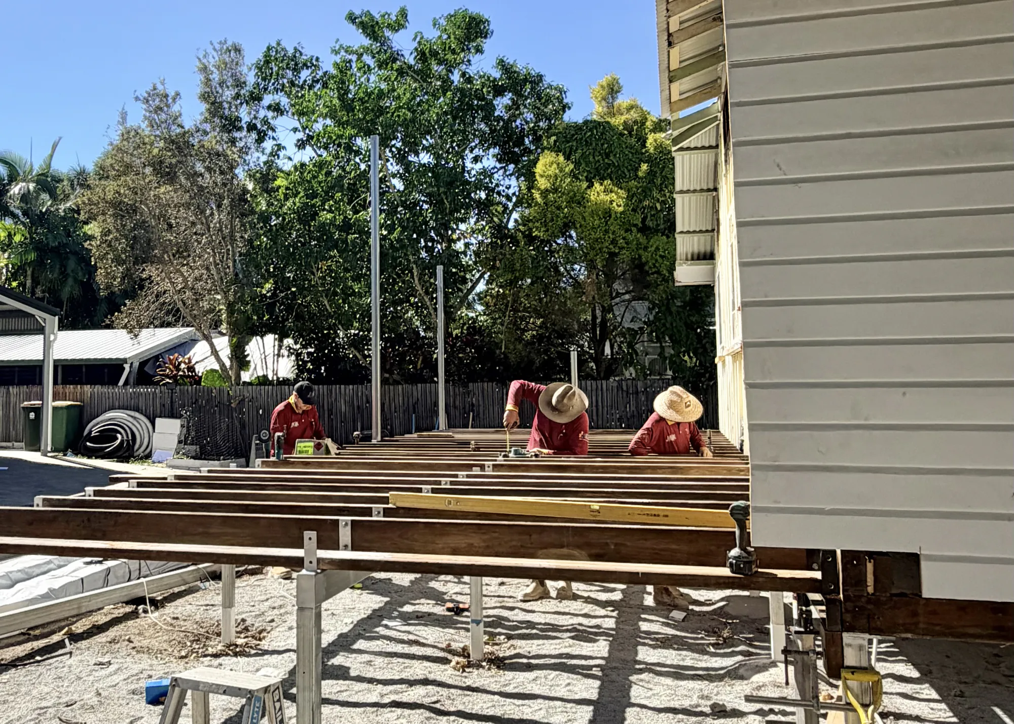 Three JKC crew in red shirts bolting up a new floor frame beside a raised house